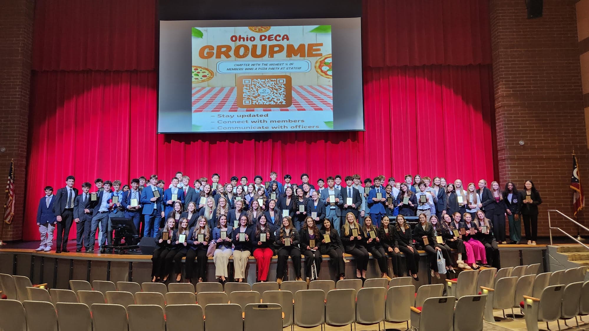 Sycamore DECA members on stage with their award plaques at a chapter ceremony
